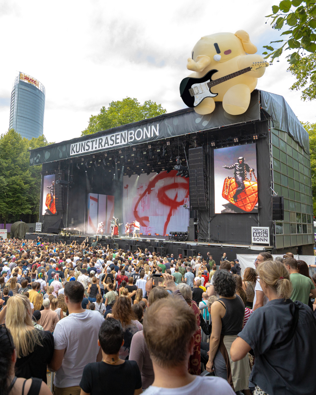 Ein Plushtodon sitzt auf der Bühne vom Kunst!Rasen und spielt Gitarre