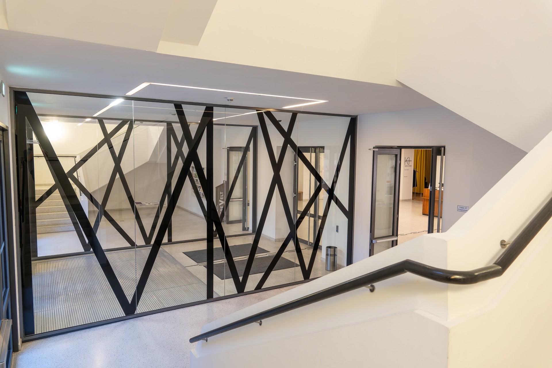 Modern gestalteter Innenbereich des Museums mit Treppe und Glaswand. Breite schwarze Linien bilden auf den Glasscheiben ein auffälliges, geometrisches Muster.