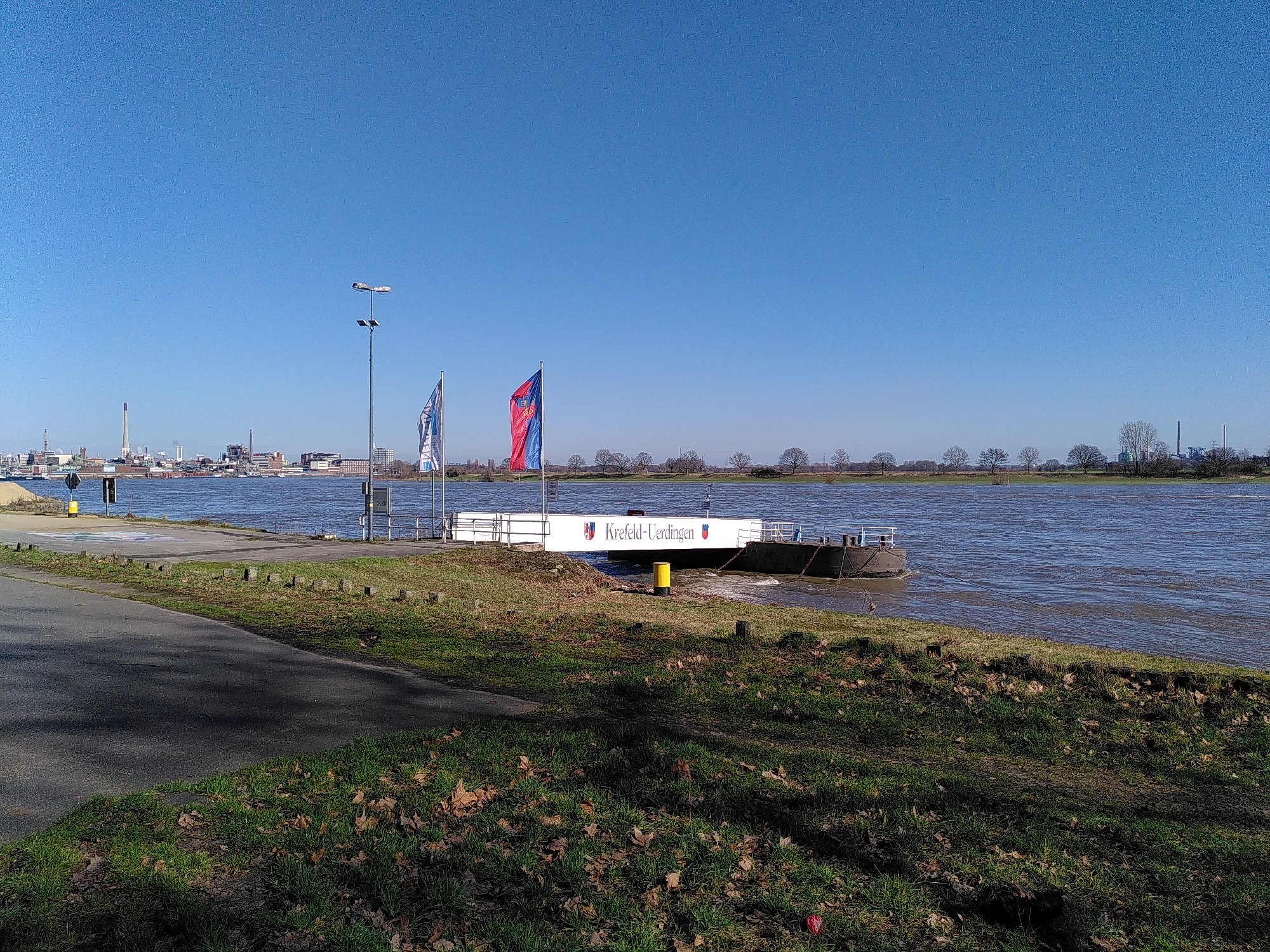 Ein Schiffsanleger mit Flaggen links und rechts. Wasser und Himmel in Bluetönen.